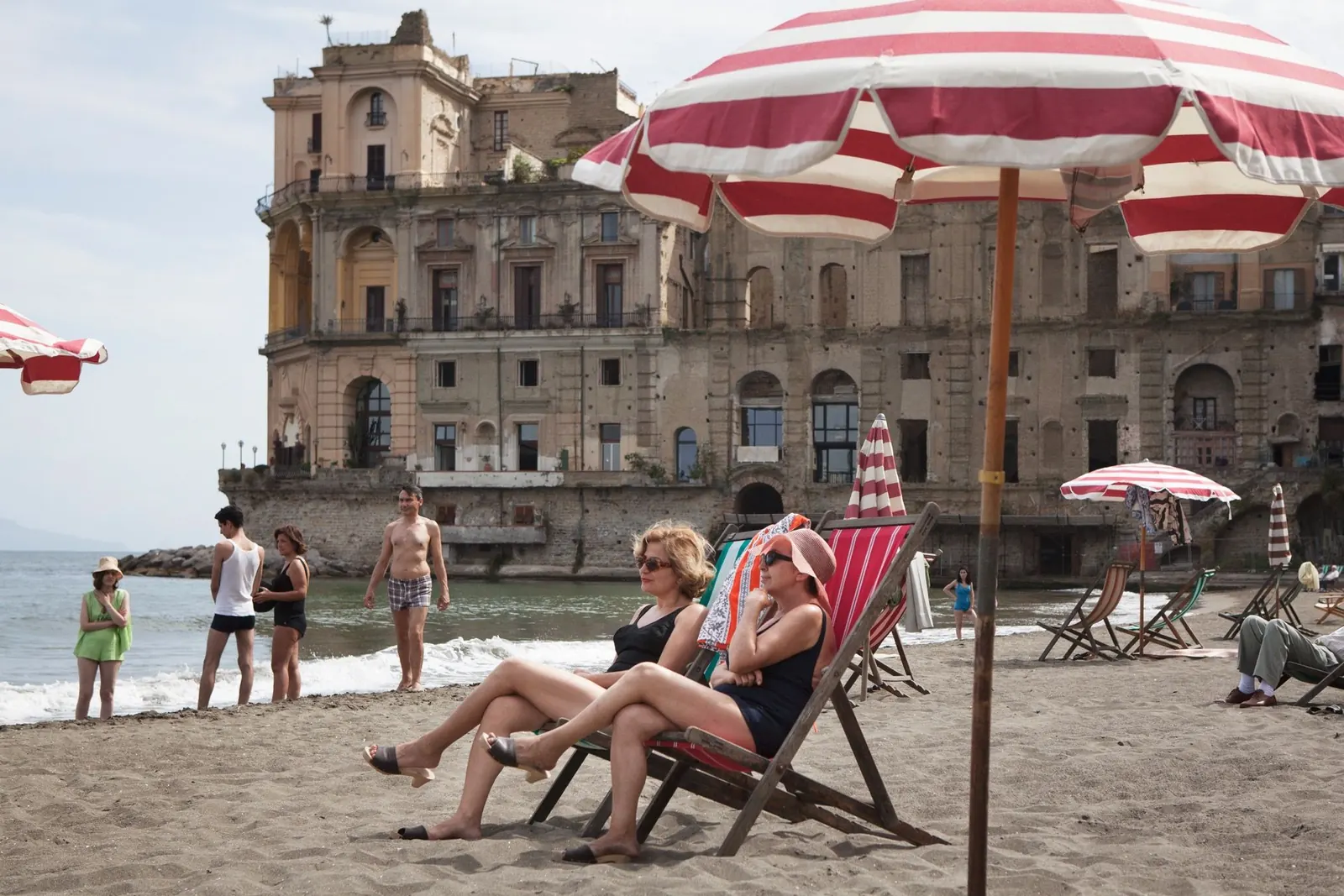 Una spiaggia di Napoli con ombrelloni e bagnanti davanti a un palazzo antico: un fotogramma di un tour VR360 di SPUN Video
